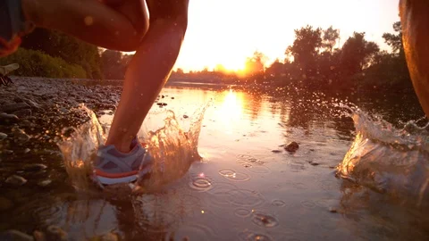 LENS FLARE: Unrecognizable couple jogging in shallow stream and towards sunset. Stock Footage 101809055