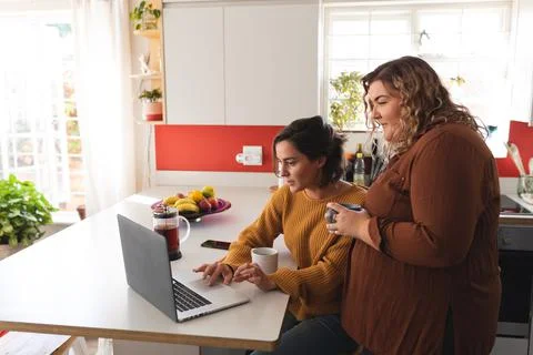 Lesbian couple smiling and using laptop in kitchen 写真素材