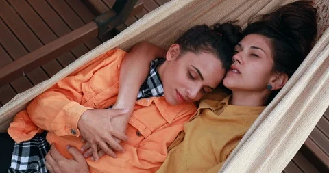Lesbian girlfriends lying on hammock cuddling and kissing each other. LGBT pr Stock Footage 126887791