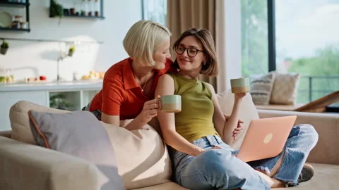 Lesbian girls looking computer modern living room. Women sitting sofa embracing Video stock 335161580