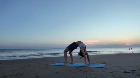 Lesbian woman practicing wheel pose yoga at sunset beach Stock Footage 327079276