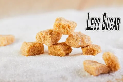 Less sugar text. Cubes of yellow sugar lying on a background of white sugar.  Stock Photos