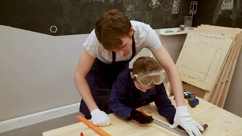 Lesson in the children's carpentry workshop, seven-year-old boy and mentor Stock Footage 102240625