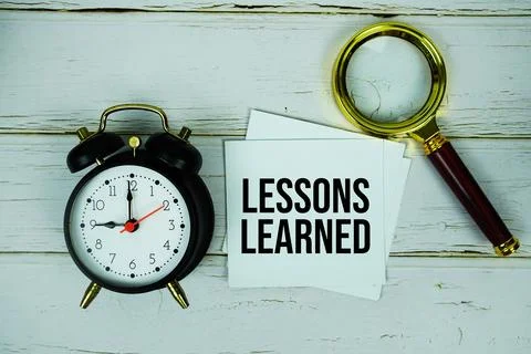 Lessons Learned text message on sticky note with magnifying glass and alarm.. Stock Photos