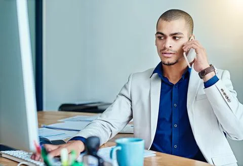 Let me confirm those details online again...a young businessman talking on a Stock Photos