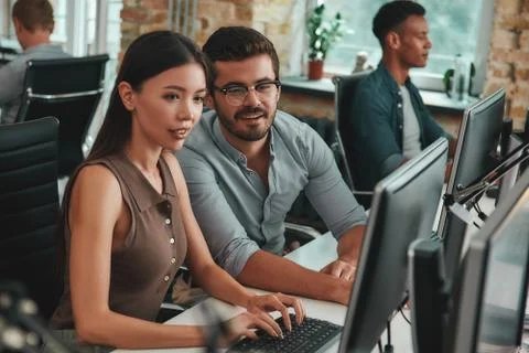 Let me explain you. Two positive young people looking at computer monitor and Stock Photos
