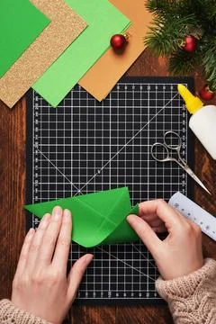 Let's make a simple paper craft. A Christmas tree bookmark. Hands fold the .. Stock Photos