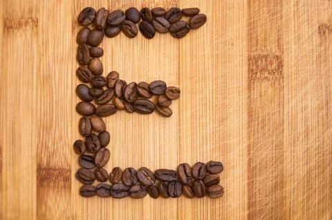 Letter E, alphabet from coffee beans. isolated on wood Stock Photos