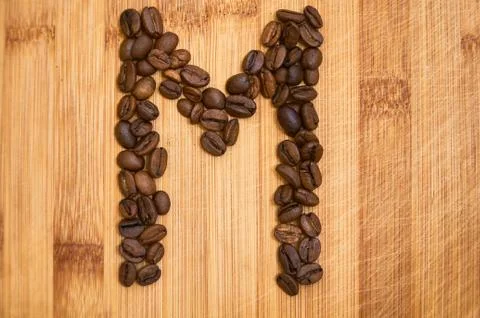 Letter M, alphabet from coffee beans. isolated on wood Stock Photos