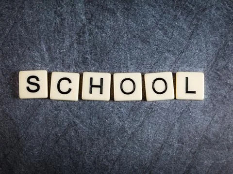 Letter tiles on black slate background spelling School Stock Photos