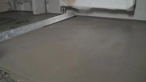 Leveling the floor with a spatula. Builder smoothing wet mortar on the floor. Stock Photos