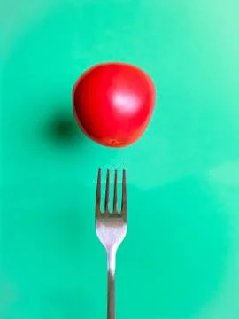 Levitating tomato over a fork on a turquoise background Stock Photos