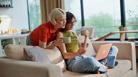Lgbt partners looking computer living room closeup. Home couple sharing coffee 스톡 동영상 335161563