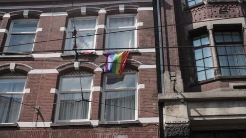 LGBTQ flag blowing in the wind underneath a window in Amsterdam Stock Footage 221729255