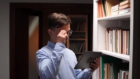 Librarian using tablet and consulting book catalog in library bookshelf Stock Footage 312284283