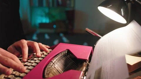 In the library man using a retro pink typewriter to type some text on the paper Stock Footage 134062135