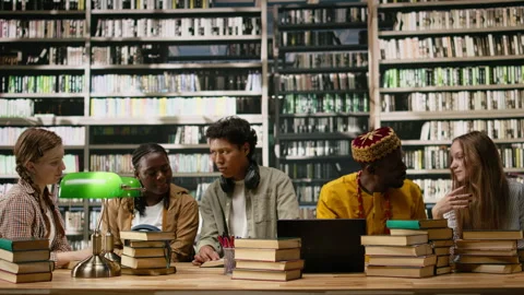 Library study group discussing ideas around laptop and stacked books Stock Footage 337229512