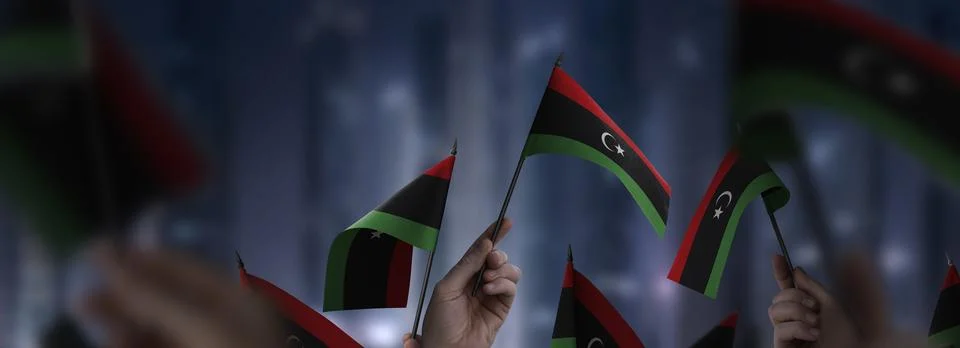 Libya flags in their hands on a blurred urban background Stock Illustration