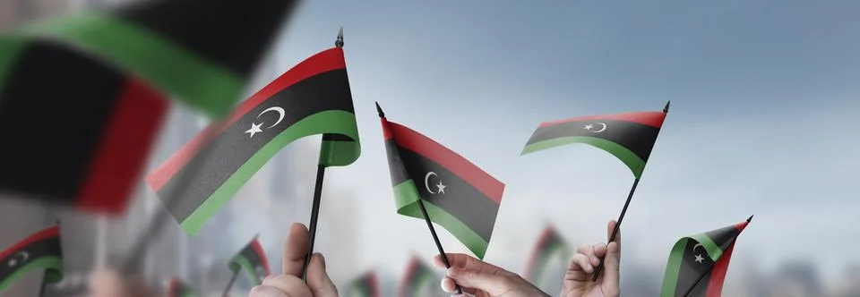 Libya flags in their hands on a blurred urban background Stock Illustration