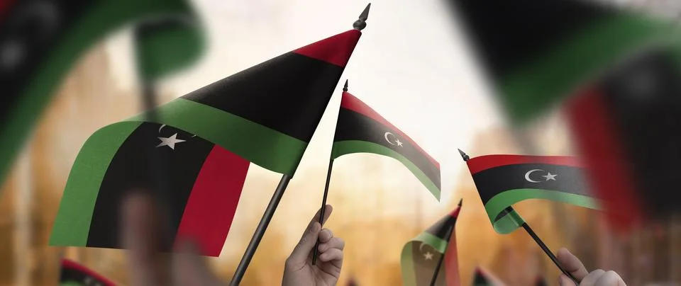 Libya flags in their hands on a blurred urban background Stock Illustration