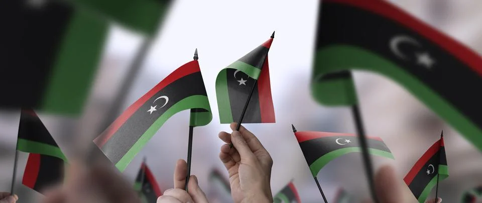Libya flags in their hands on a blurred urban background Stock Illustration