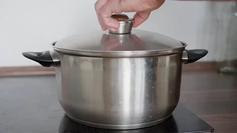 Lid is placed on a metal pot with boiling broth soup on a stovetop. Close-up of Video stock 317779625