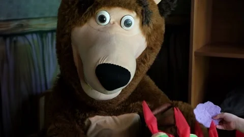 Life-size puppet of a brown bear sits in a cozy armchair and eats sweets. High q Stock Footage 160976544