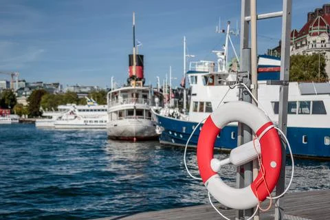 Lifebelt on a pier with boats and ferries in the background Stock Photos