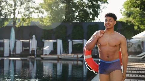 Lifeguard man standing at resort pool, holding red lifebuoy for safety on water Stock Footage 333565016