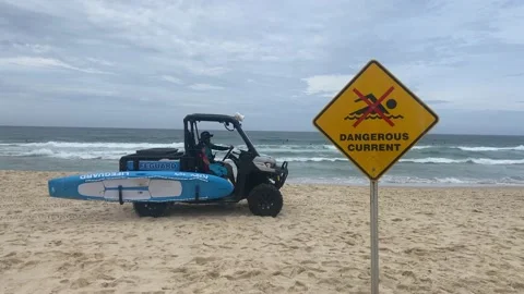 A lifeguard riding a beach buggy in front of Sydney Dangerous Current Sign Board Stock Footage 219664789
