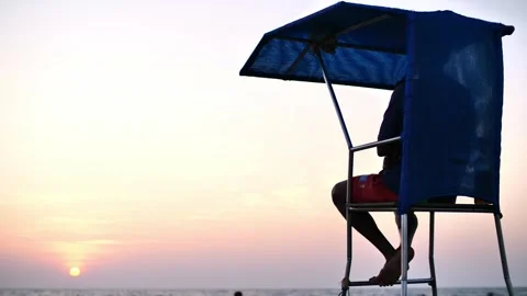 Lifeguard sitting on a tower on the beach at sunset Stock Footage 264088852