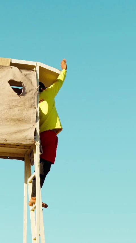 A lifeguard on a tower on a sandy beach monitors the safety of people at sea. Video stock 328002314