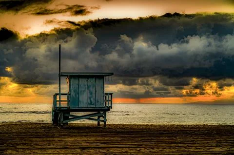 Lifeguard tower stands against dramatic sunset clouds over the ocean Stock Photos
