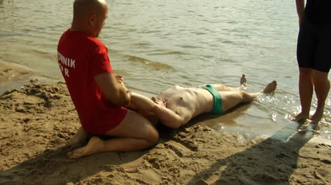 Lifeguards pulling unconcious man from the water, checking for injuries Stock Footage 39477545