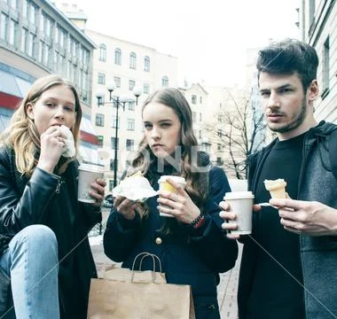 Lifestyle and people concept: two girls and guy eating fast food on city street Stock Photos