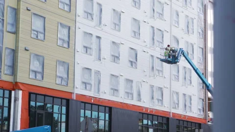 A lift carries construction workers up the side of a new apartment building Stock Footage 274555294