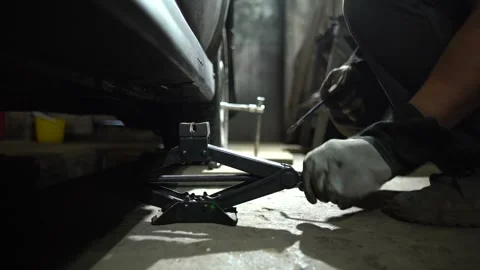 Lifting the car using a jack for maintenance. Protective gloves are worn for Stock Footage 332227178