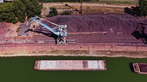 Lifting cargo at a river dock with a crane and barge near a storage area Stock Footage 343125544