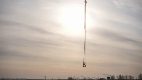Lifting crane chain hooks move against tower and sunset Stock Footage 125930417