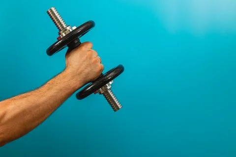 Lifting a dumbbell against a solid blue backdrop Stock Photos