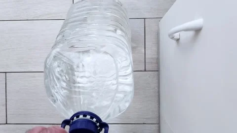 Lifting a Large Water Bottle Next to a White Toilet in a Bathroom Setting 스톡 동영상 314934493