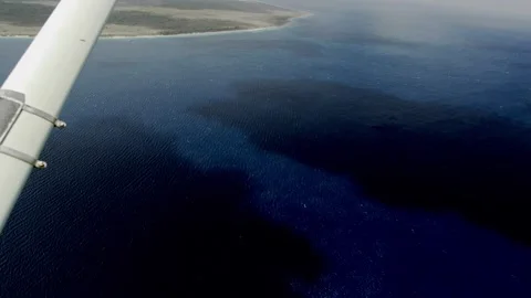 Light aircraft wing over deep blue ocean and reef patterns, Bonaire Stock Footage 343774319