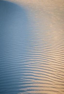 Light and pattern on wave shapes at white sand dune at sunset Stock Photos