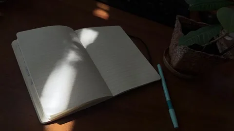 Light beam shifting across open notebook on wooden desk Stock Footage 336233988