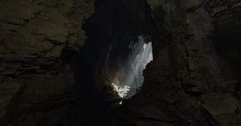 Light beams illuminate dark cave interior with rocky formations Stock Illustration