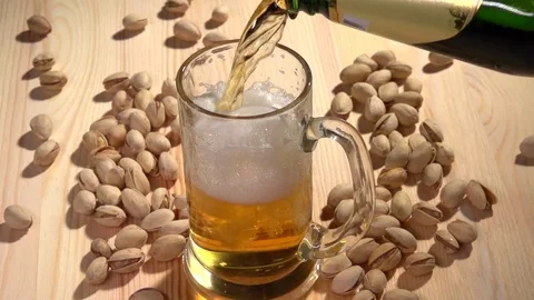 Light beer is poured into a glass on the table with crumbled pistachios. Video stock 70959356