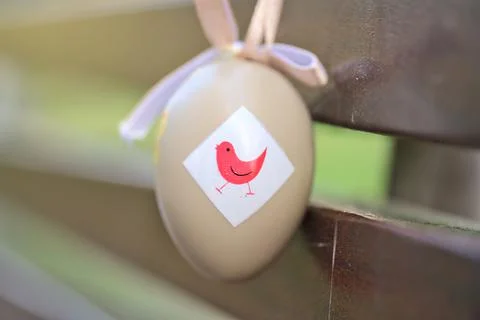 Light beige plastic decorative Easter egg tied with ribbon on dark brown bench Stock Photos