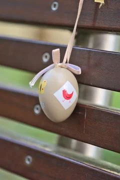 Light beige plastic decorative Easter egg tied with ribbon on dark brown bench Stock Photos