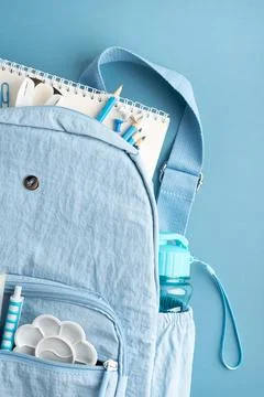 Light Blue Backpack Filled With School Supplies And Water Bottle On Blue Ba.. Stock Photos