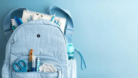 Light blue backpack filled with school and art supplies on a light blue bac.. Stock Photos
